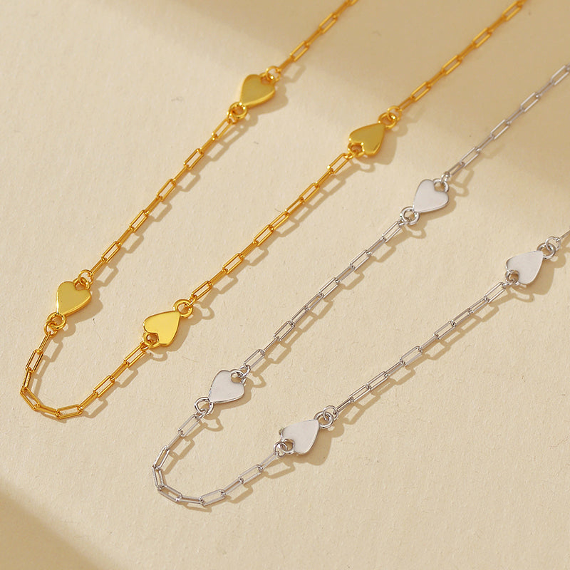 Two gold and silver heart-shaped chain necklaces on a beige background