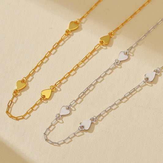 Two gold and silver heart-shaped chain necklaces on a beige background